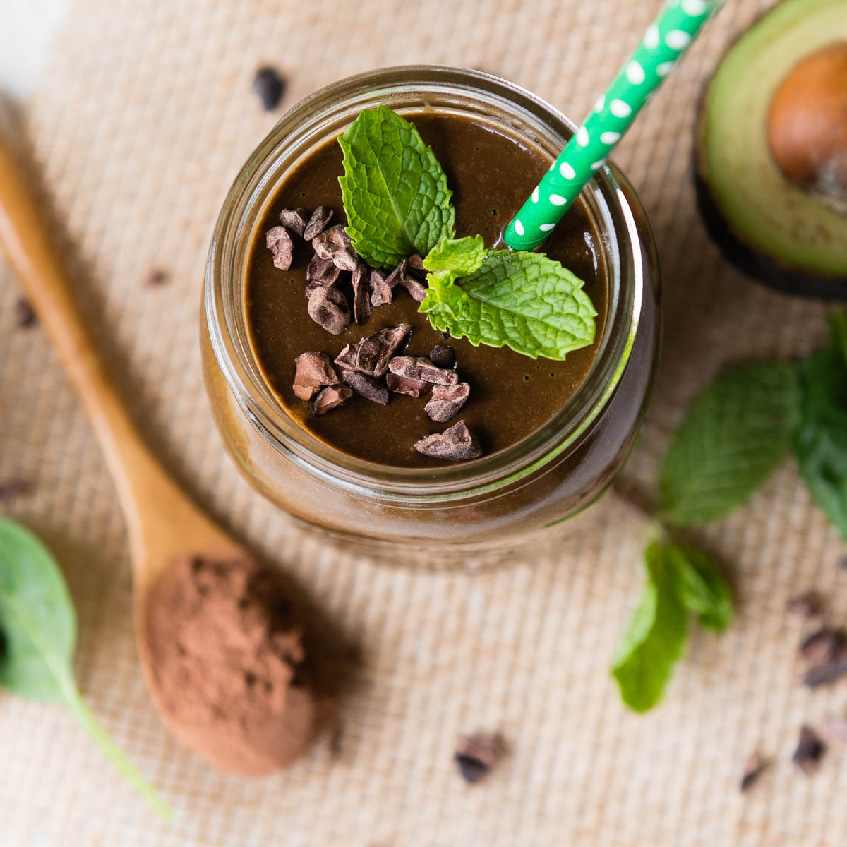 energizing mint chocolate smoothie topped with fresh mint and cacao nibs with a green straw.