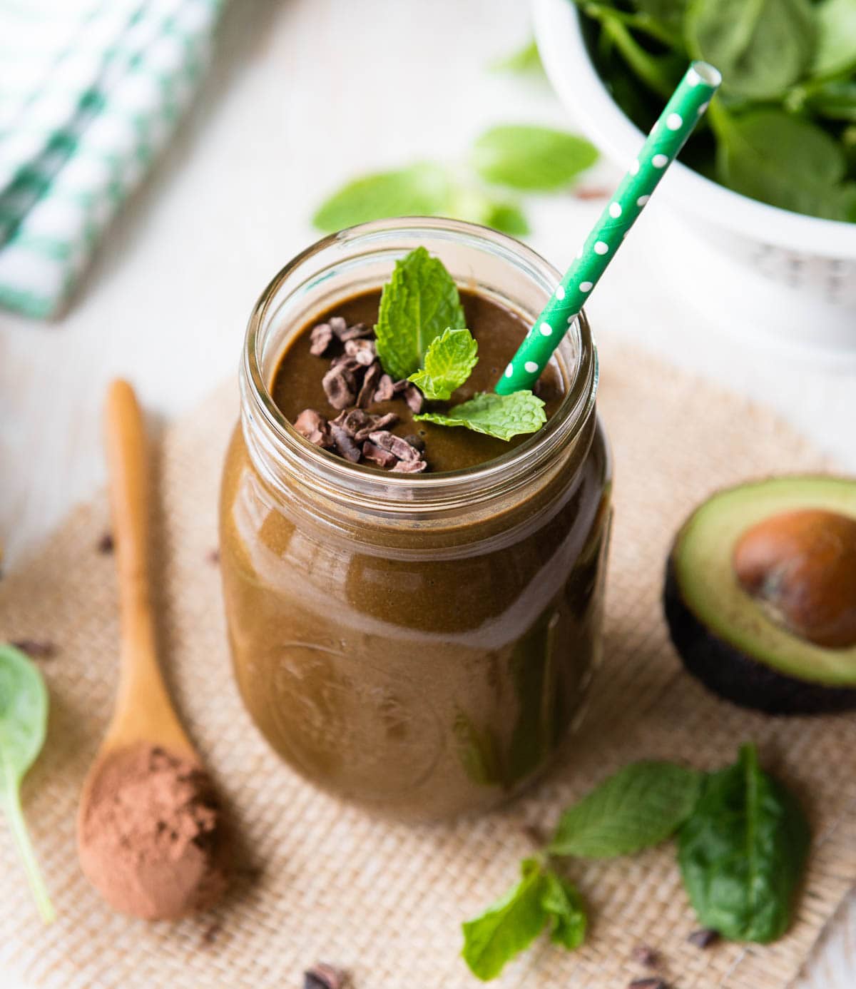 photo of mint chocolate protein shake in a glass jar surrounded by avocado, mint leaves and cacao powder