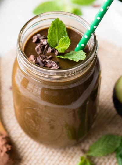 photo of a mint chocolate smoothie in a glass jar with a paper straw topped with fresh mint and cacao nibs
