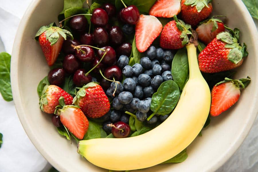 bowl of spinach, strawberries, cherries, blueberries and banana.