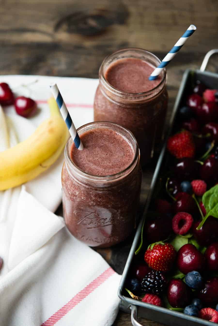 2 deep red smoothies with paper straws in glass jars.