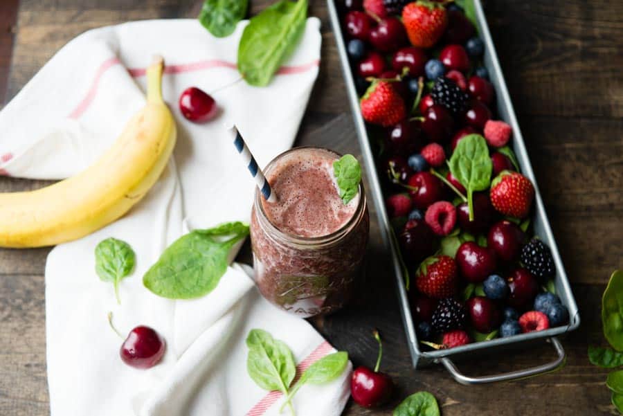 glass jar of green smoothie with a paper straw next to a container of fresh berries.