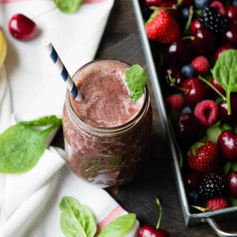Mixed berry smoothie in a glass jar with a paper straw, next to a container of fresh mixed berries.