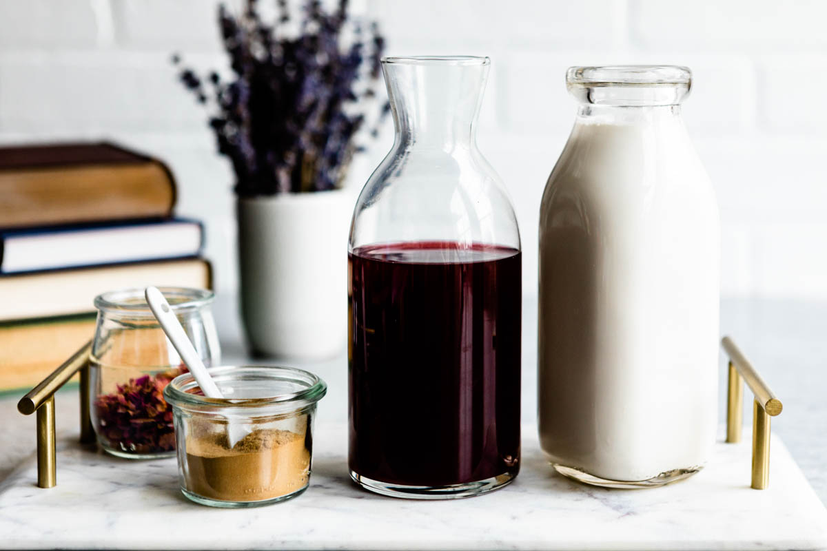 ingredients for a moon milk recipe including cherry juice, cashew milk, cinnamon and dried flowers.