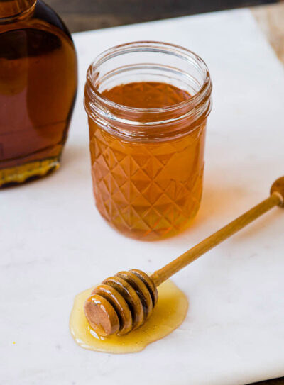 examples of natural sweeteners including bananas, honey in a glass jar, maple syrup and dates.