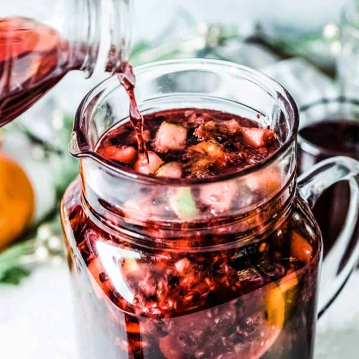 non alcoholic berry sangria poured into a glass pitcher with floating fresh fruit.