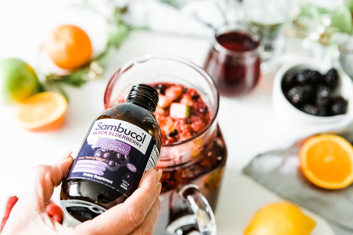 A person pouring black elderberry syrup in a sangria drink
