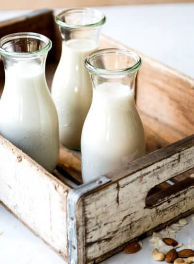 Three glass bottles of plant-based non-dairy milk in a rustic wooden crate.