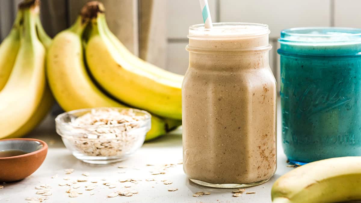 Healthy banana oatmeal smoothie in a jar with bananas and oats in the background.
