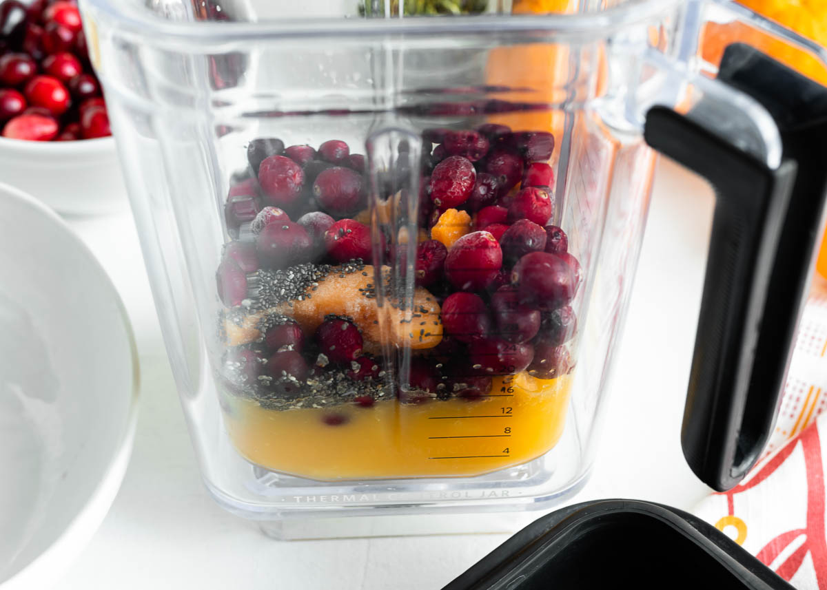 blender container full of frozen fruits and orange juice for a smoothie.