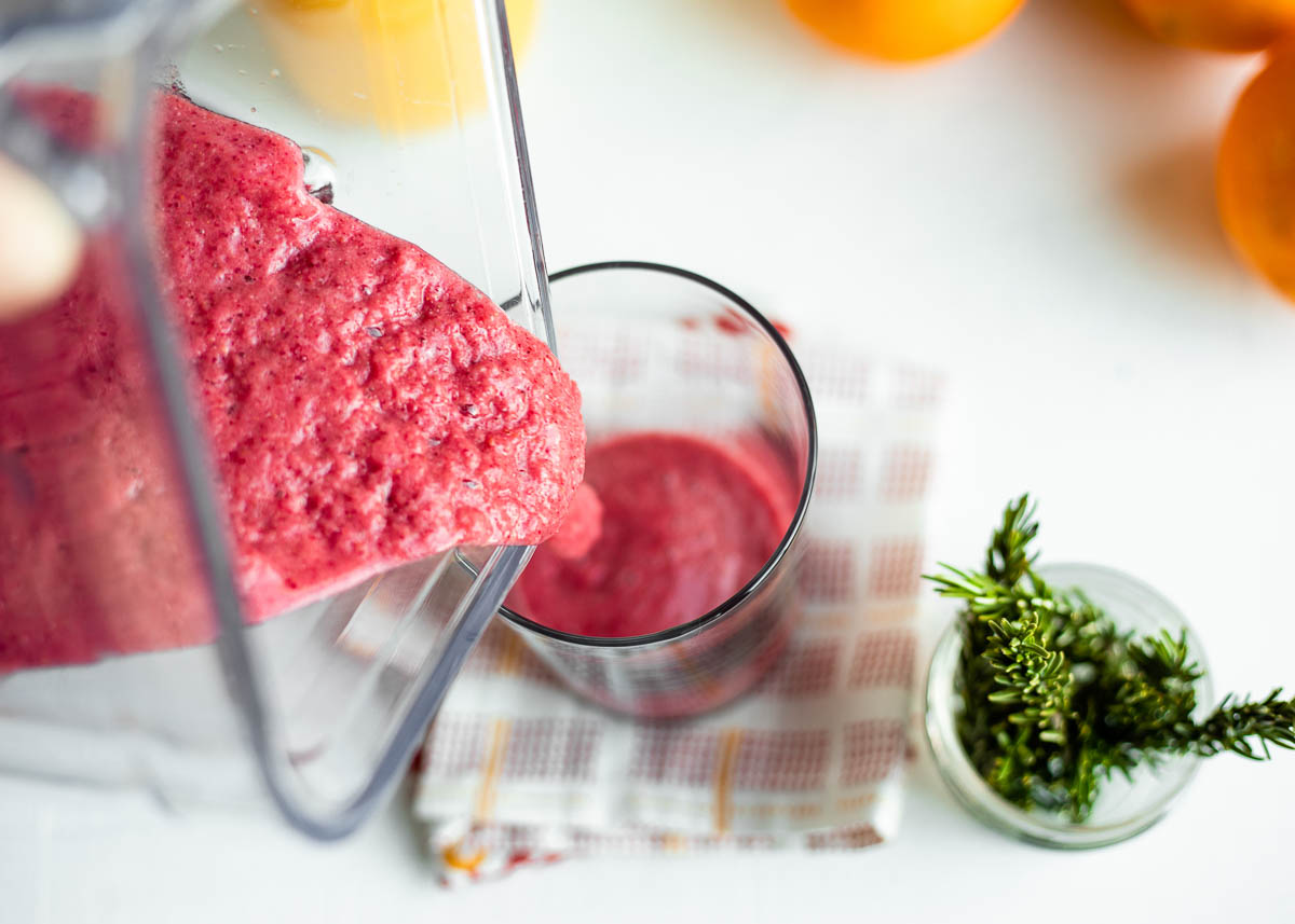 An orange cranberry smoothie poured from a blender into a glass. 