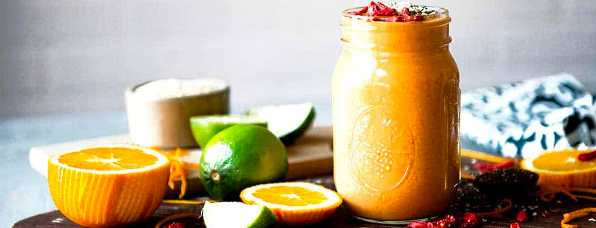 orange smoothie from the side in a jar with citrus that has been zested sitting around it