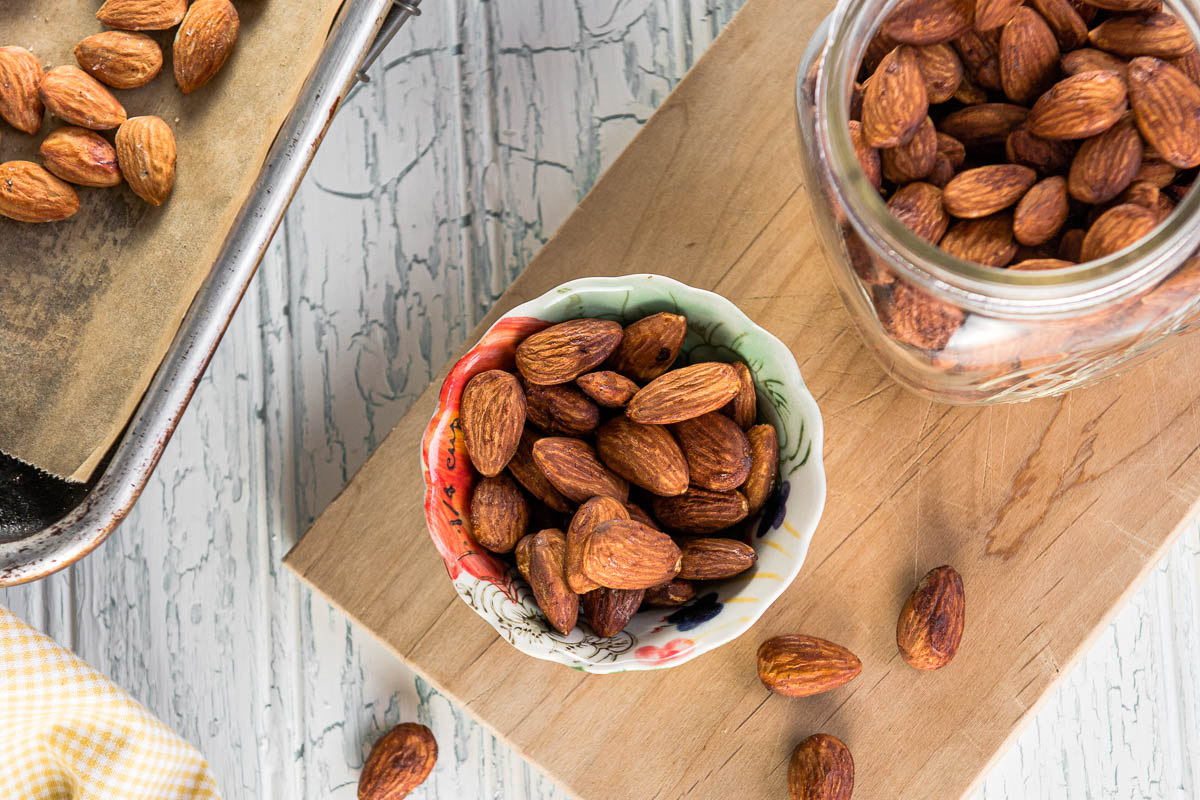 tamari almonds in a colorful bowl and in a glass jar on a wooden cutting board.