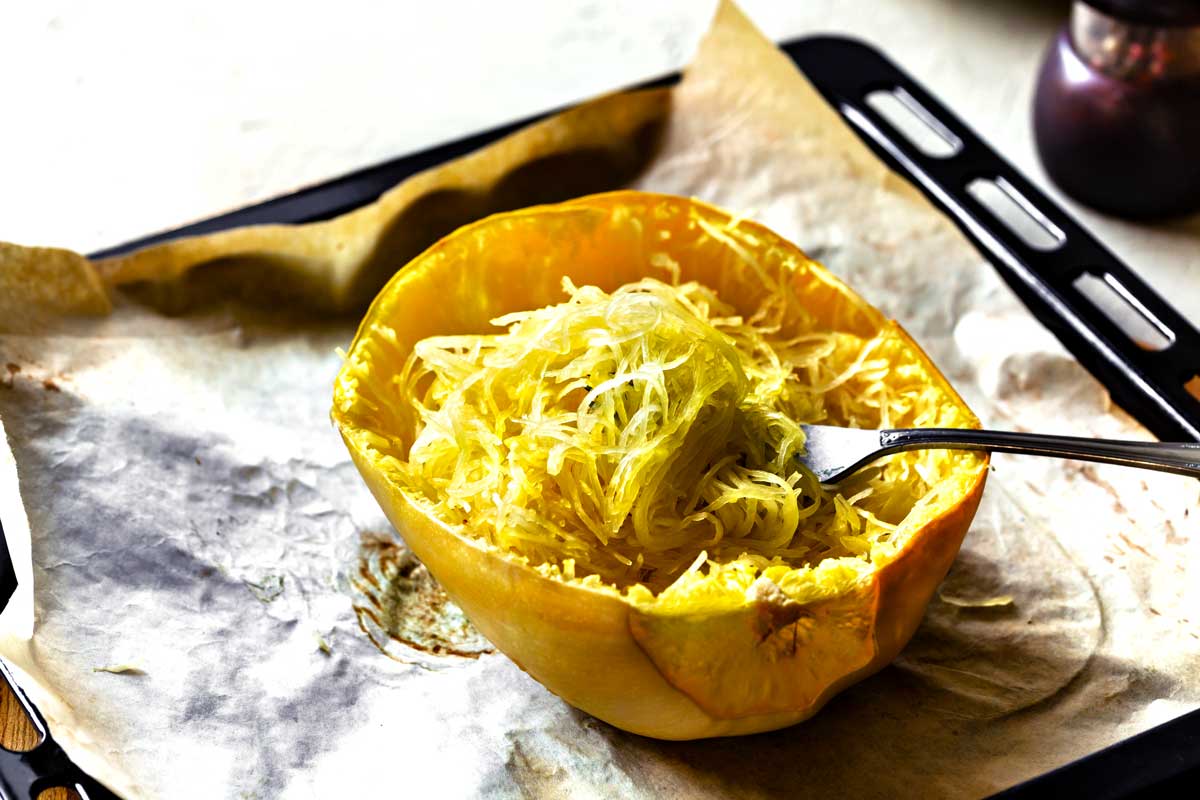 Baked spaghetti squash on tray with fork shredding the flesh to create noodles