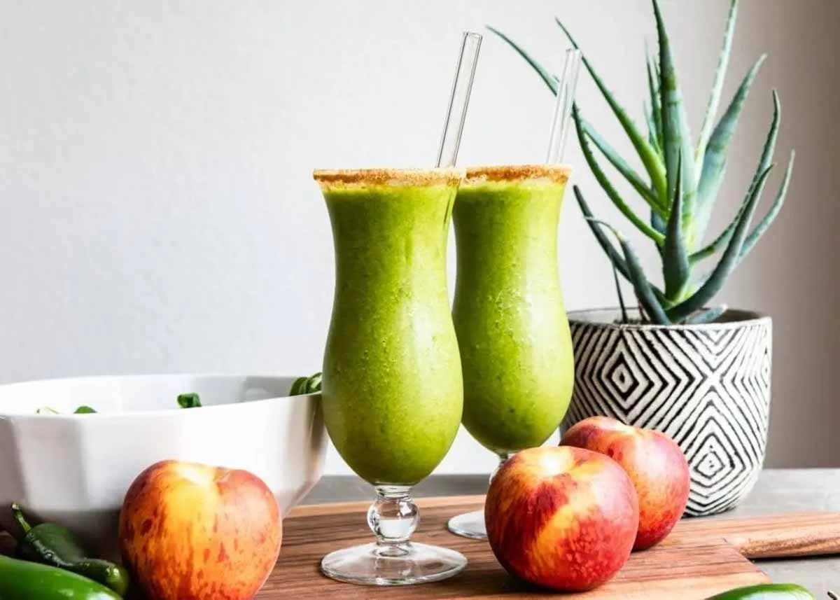 2 green smoothies in cocktail glasses with glass straws and rimmed with coconut sugar.