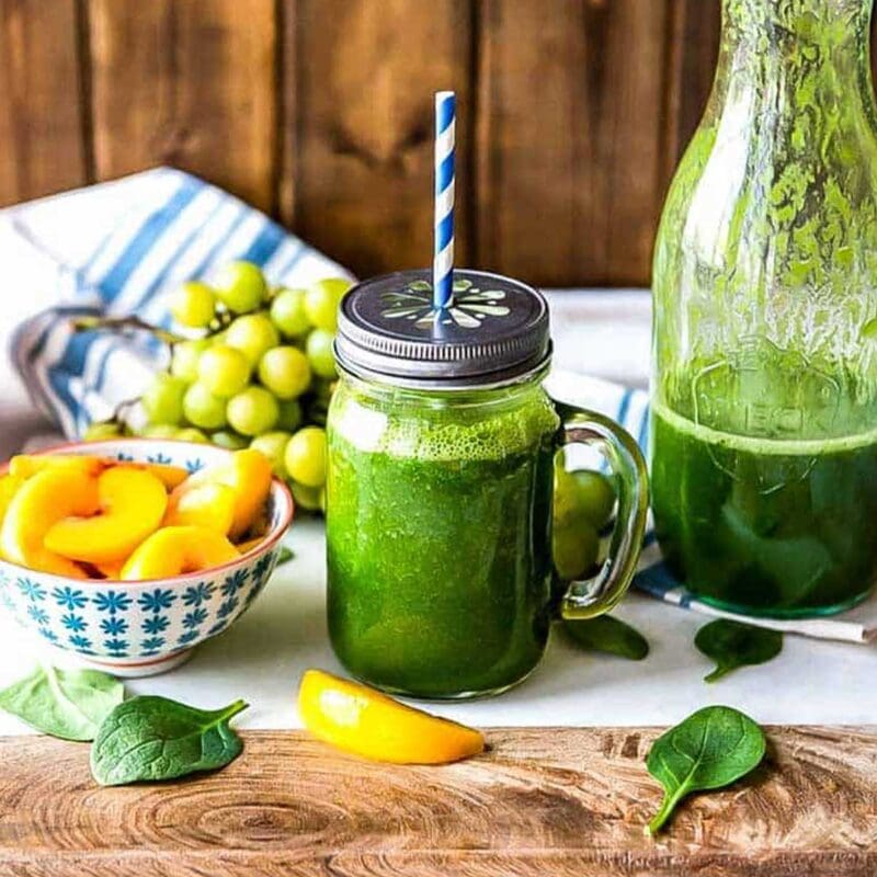 green smoothie in a glass jar with a daisy cut lid and a paper straw.