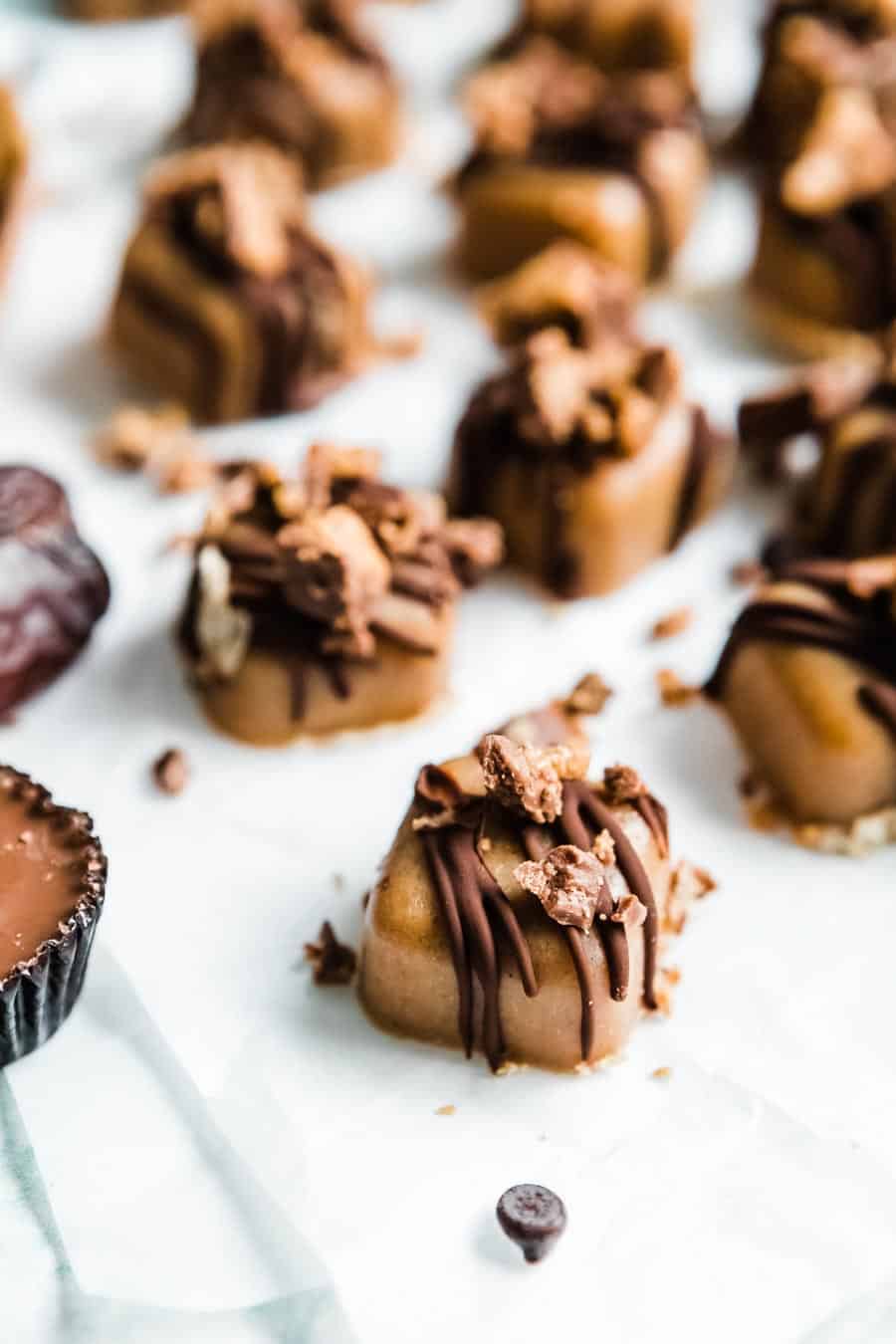 peanut butter fudge squares topped with chocolate and vegan peanut butter cup crumbles on white parchment.