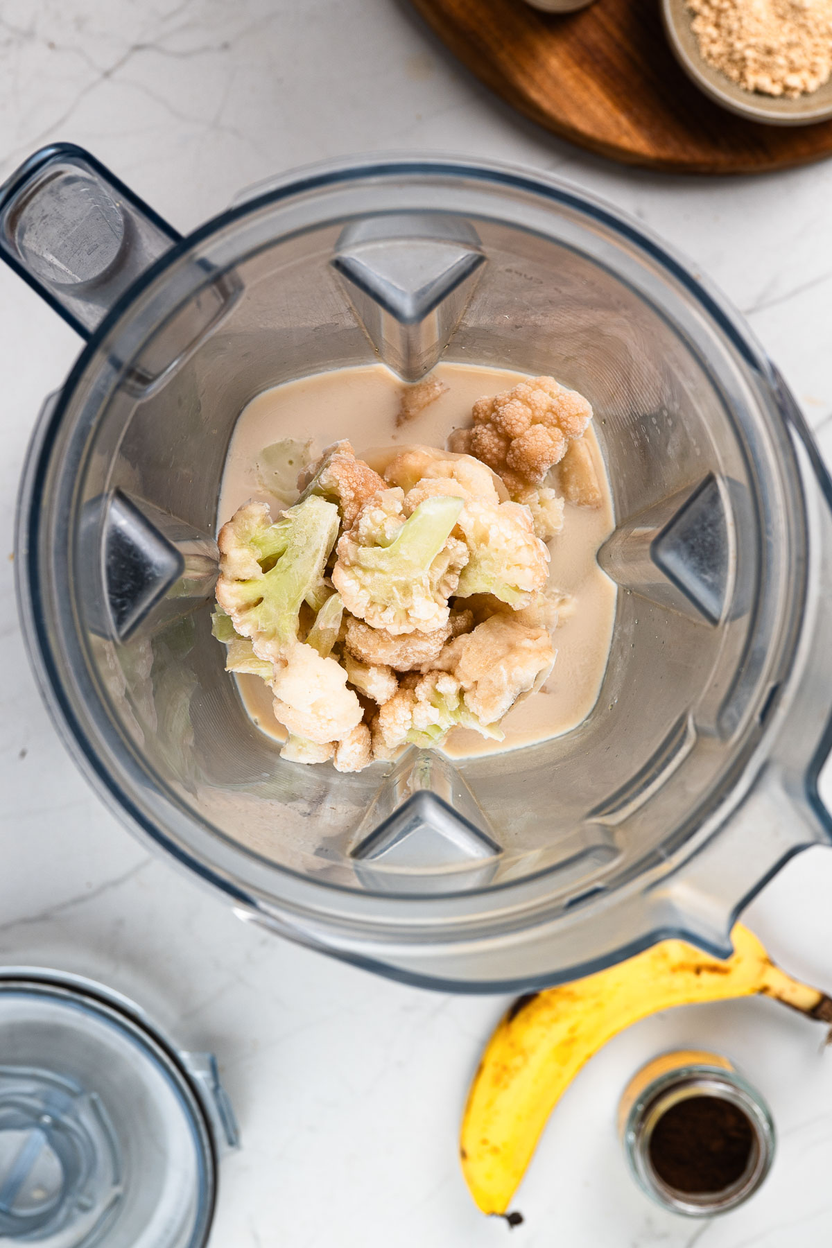 Oat milk, banana, and cauliflower ready to blend in a high-speed blender