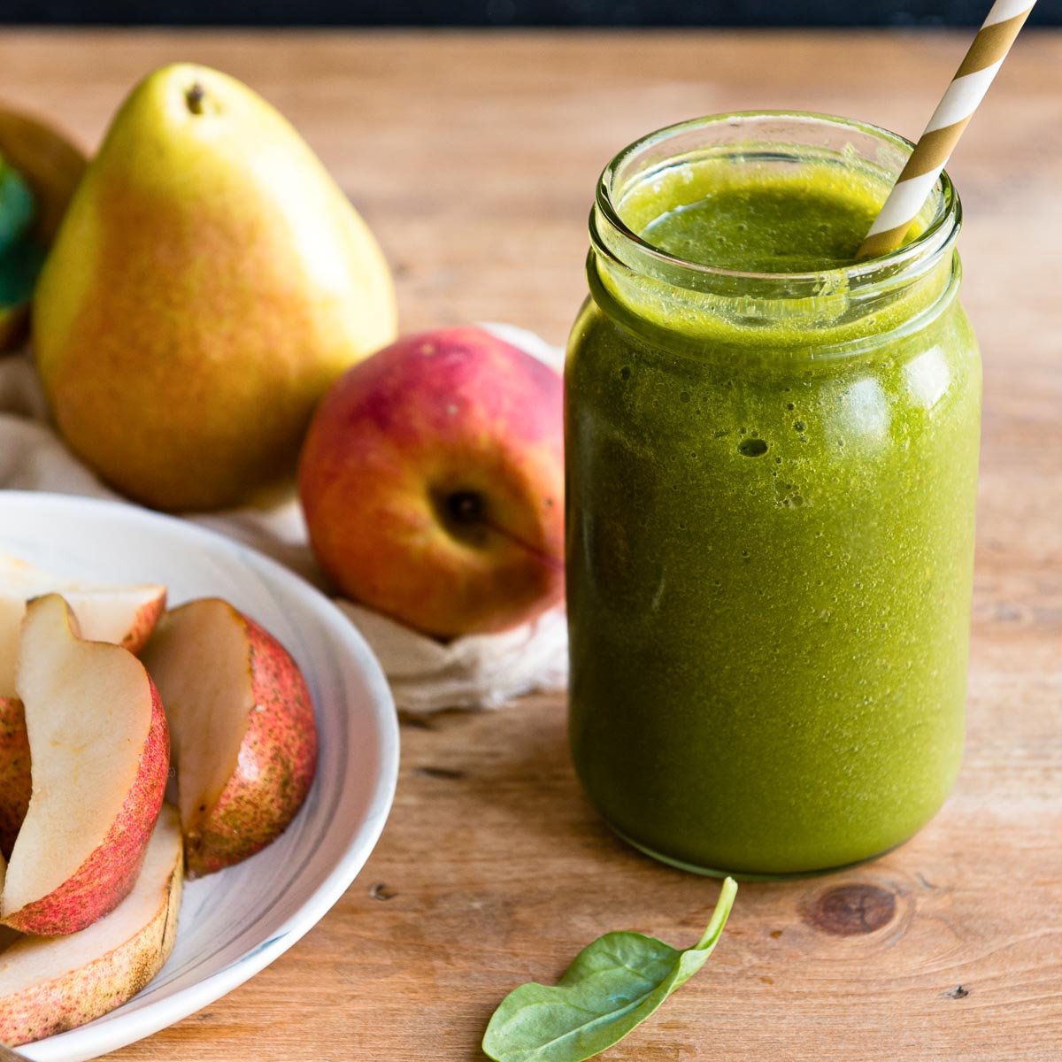 green pear smoothie in a mason jar with a paper straw, next to some sliced and whole pears.