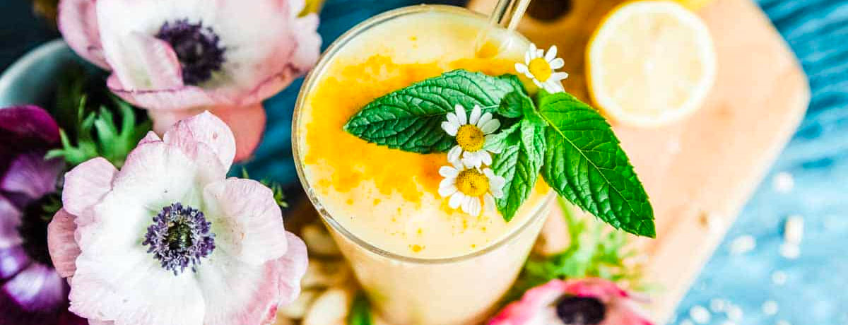 yellow smoothie with herbs and flowers on top and flowers in the background