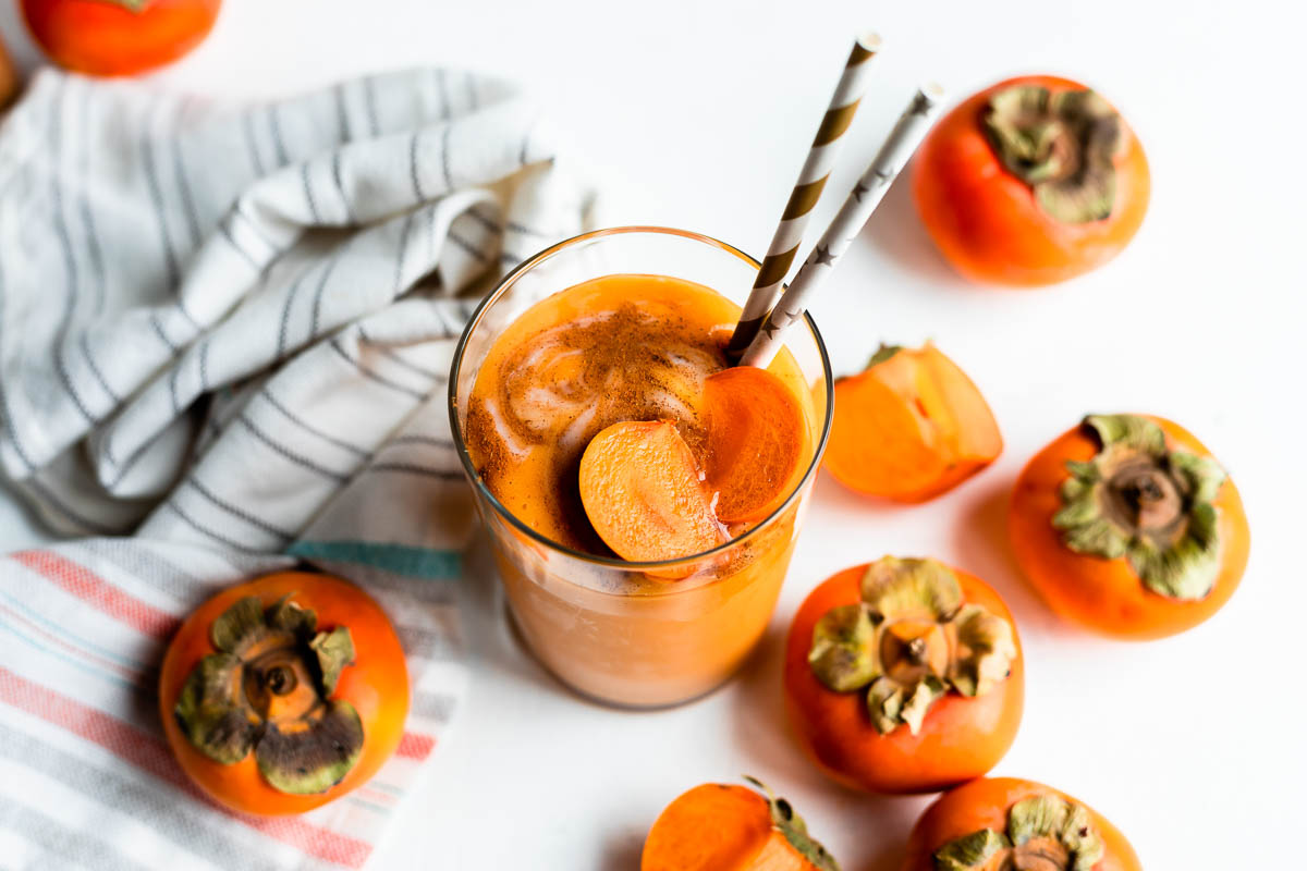 glass full of orange smoothie topped with orange fruit, cinnamon and 2 paper straws.