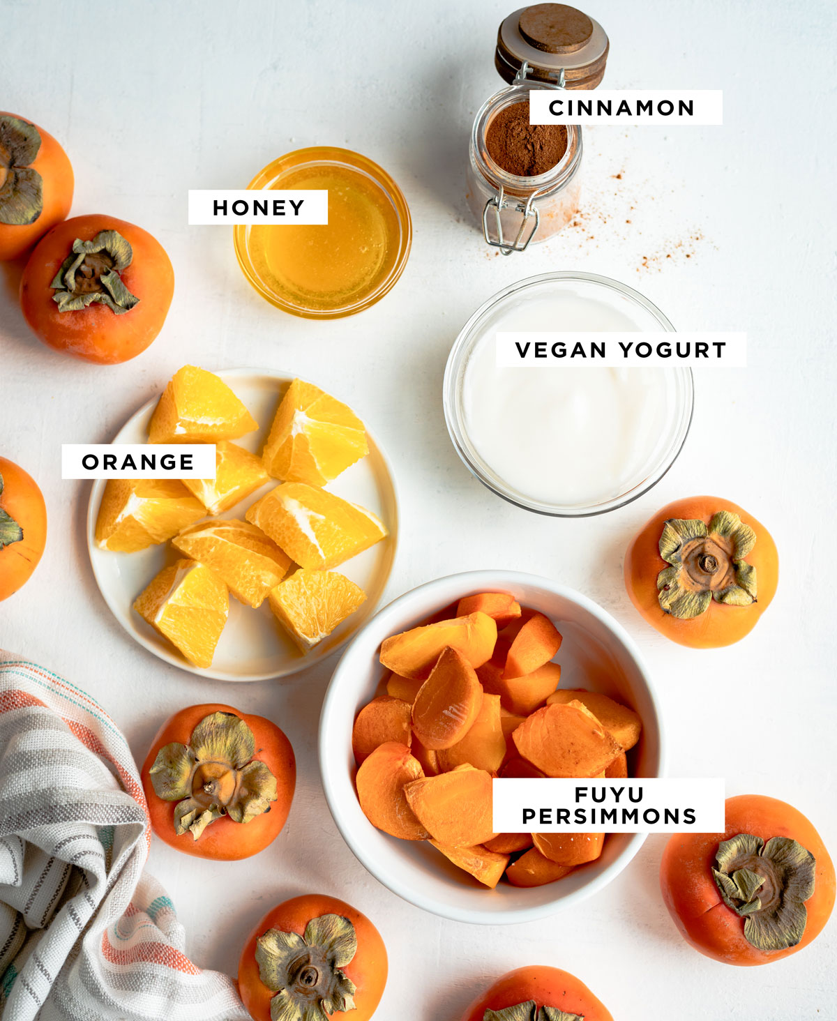 labeled ingredients for a persimmon smoothie including cinnamon, honey, vegan yogurt, orange and Fuyu persimmons.