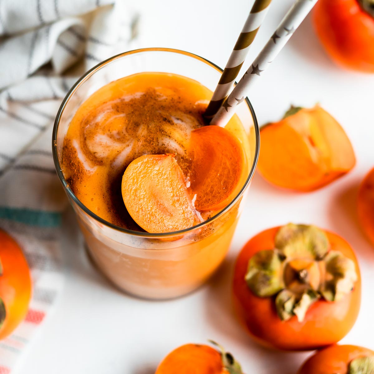 Persimmon smoothie with a scoop of yogurt in a glass with a paper straw.