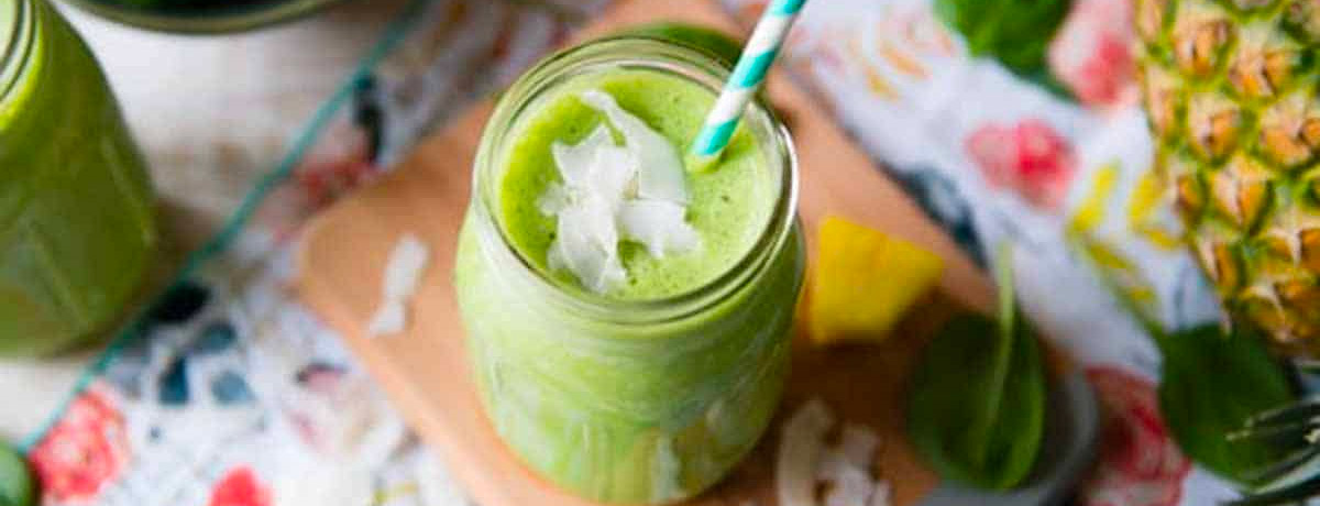 green smoothie with coconut flakes on top and a bright blue straw with pineapple to the side