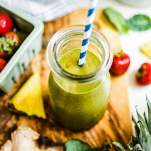 A pineapple ginger smoothie in glass jar with a straw.