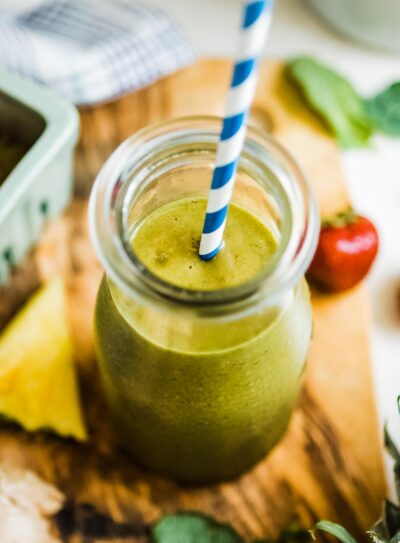 A pineapple ginger smoothie in glass jar with a straw.