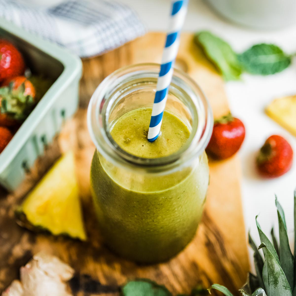 A pineapple ginger smoothie in glass jar with a straw.