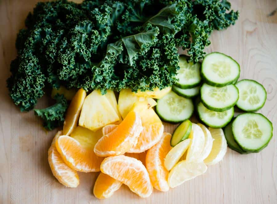 ingredients for a pineapple green smoothie including kale, cucumber, pineapple, orange and lemon.