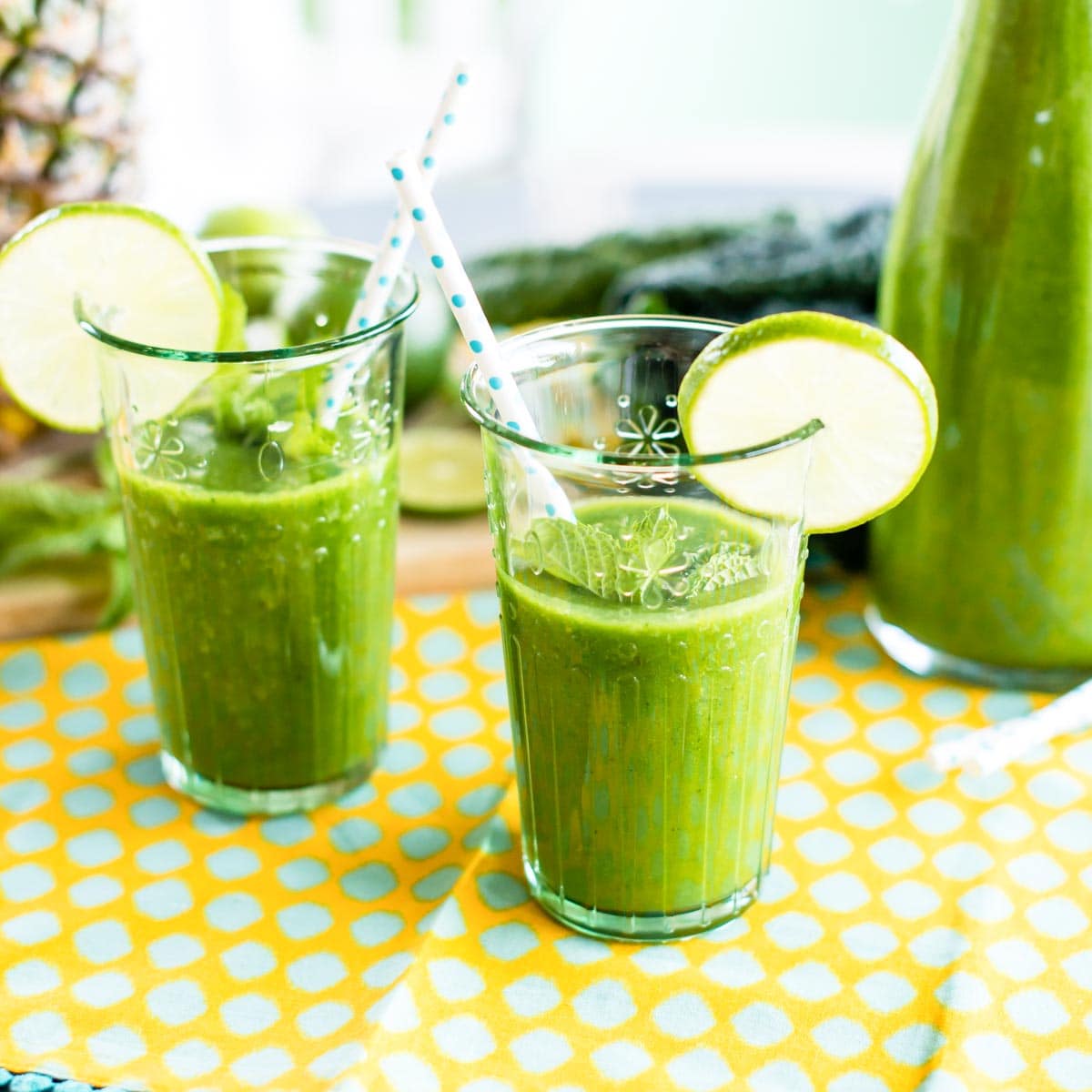 2 glasses of pineapple mint smoothie in glasses with lime wedges.