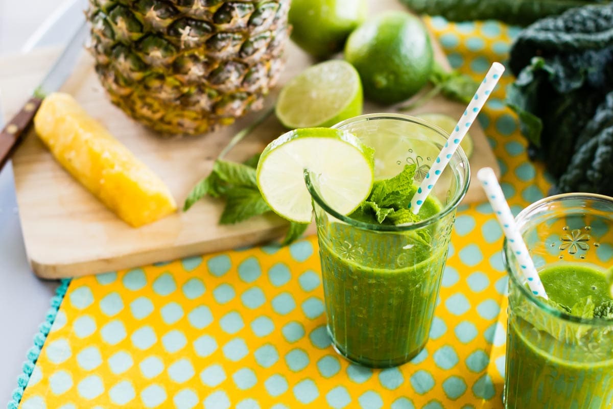 pineapple mint smoothie in a glass with a paper straw and a lime wedge.