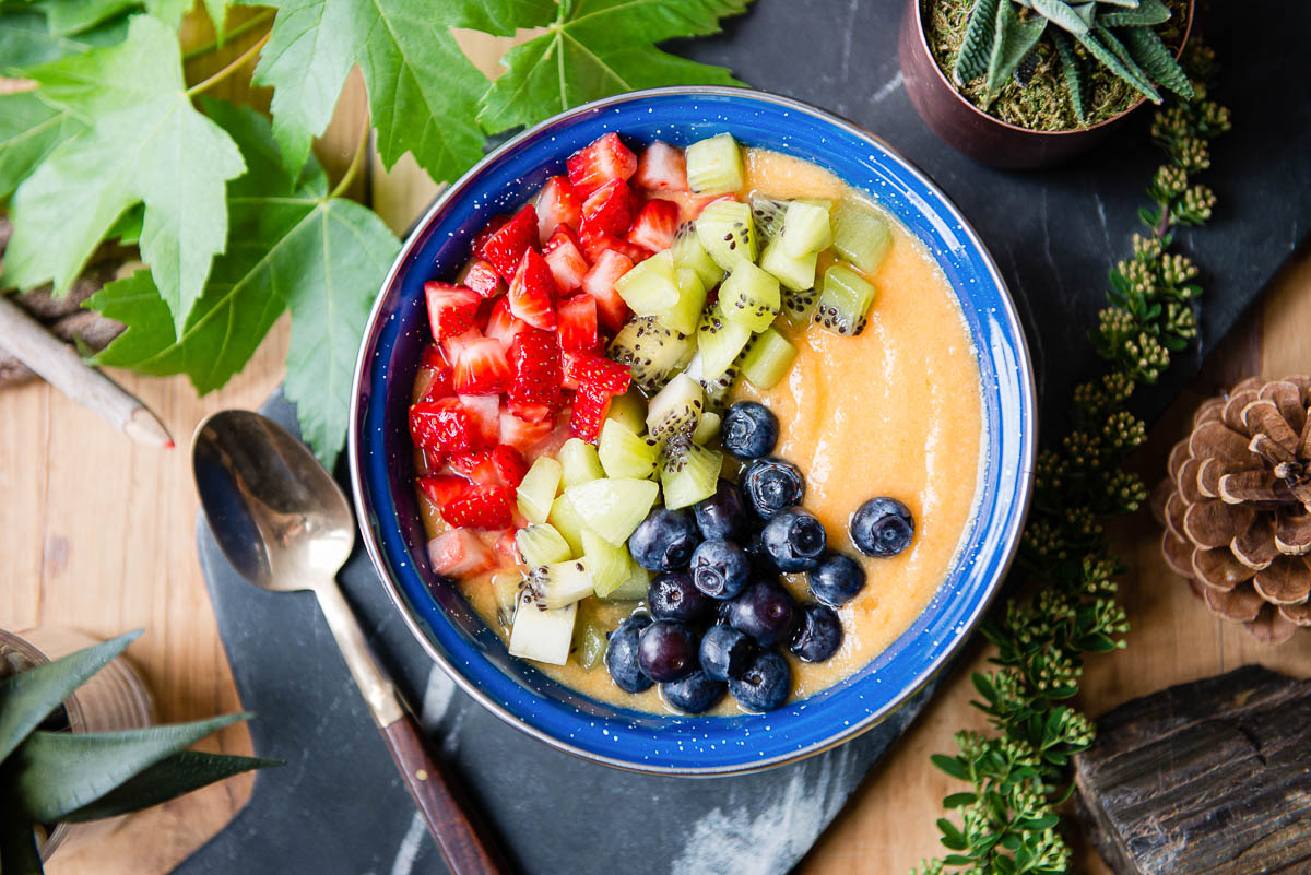pineapple smoothie bowl topped with strawberries, kiwi and blueberries in a blue bowl.
