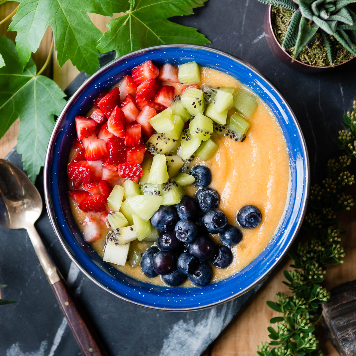 bright blue bowl of orange smoothie topped with fresh fruit.