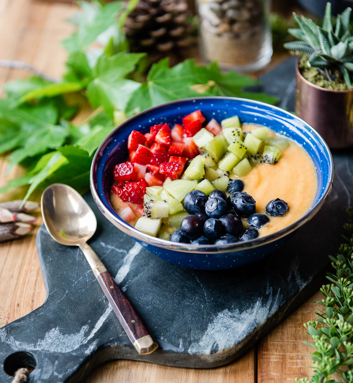 pineapple smoothie bowl topped with fresh fruit on a gray slab next to a spoon.