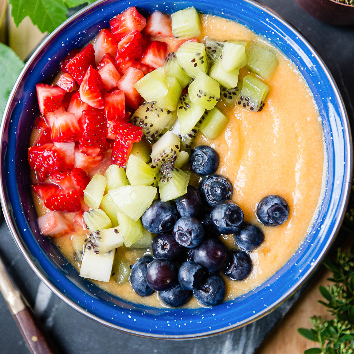 Pineapple smoothie bowl topped with chopped strawberries, kiwi, and blueberries.