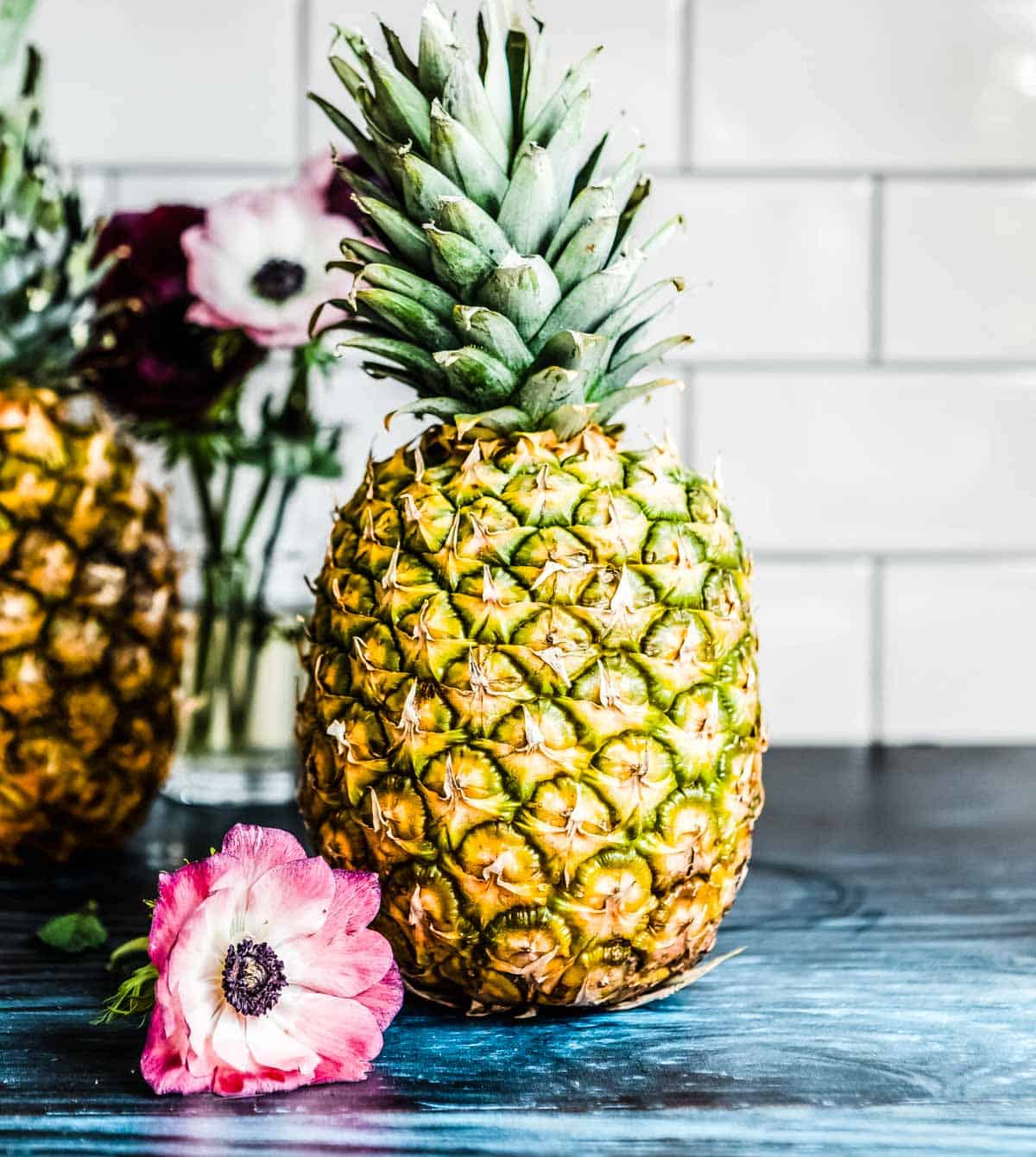 whole pineapple next to a pink and white flower.