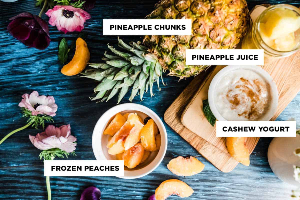 Labeled ingredients for an easy pineapple smoothie, including pineapple chunks, pineapple juice, cashew yogurt, and frozen peaches.