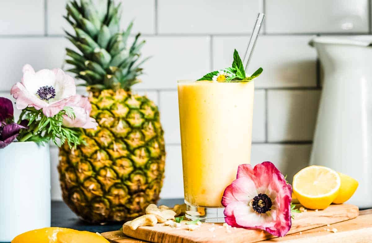 pineapple smoothie in a glass with a glass straw on a counter top.