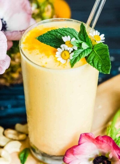 pineapple smoothie in a glass with a glass straw and mint garnish.