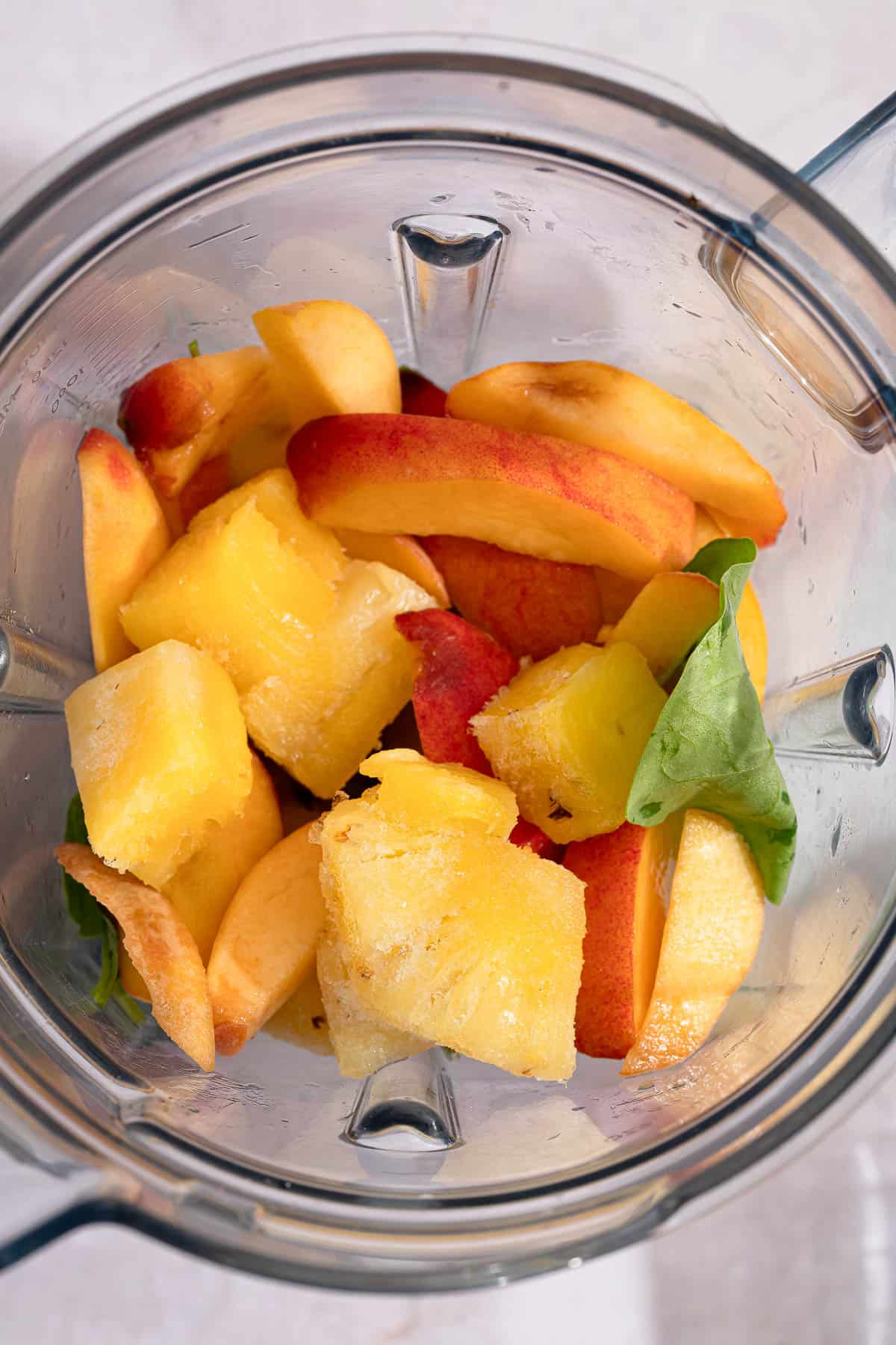 Frozen pineapple and peach chunks in a blender with spinach.