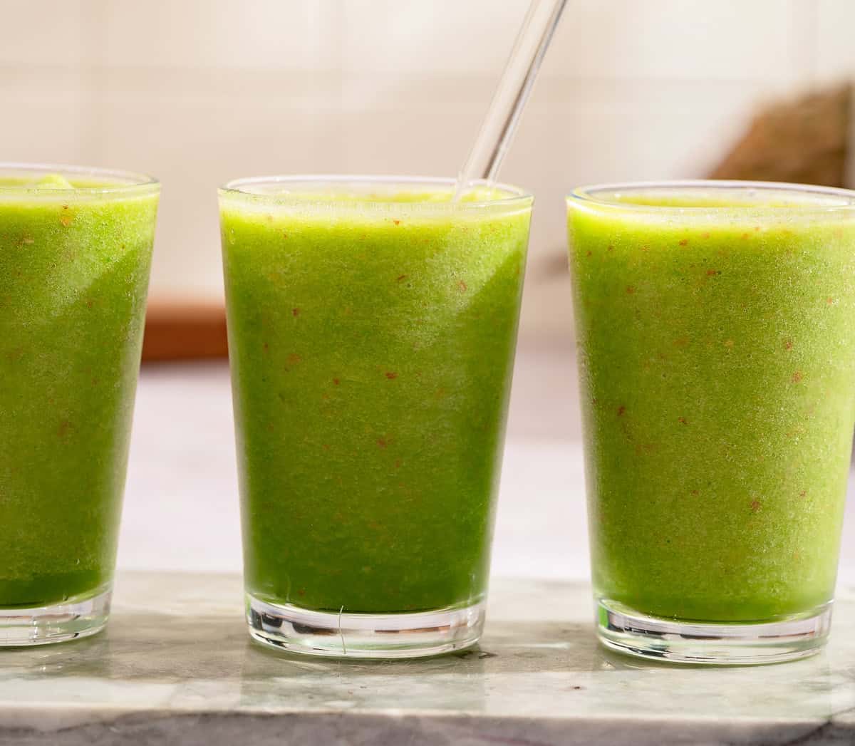 Three glasses of vibrant green pineapple spinach smoothies