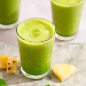 Fresh green pineapple spinach smoothie in a glass with pineapple pieces nearby.