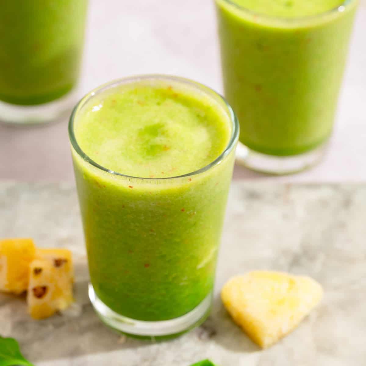 Fresh green pineapple spinach smoothie in a glass with pineapple pieces nearby.
