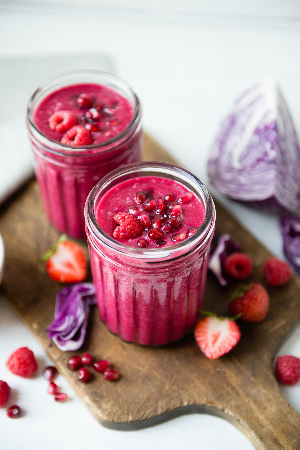 two glass jars of red fruit smoothie topped with raspberries and pomegranate arils. 