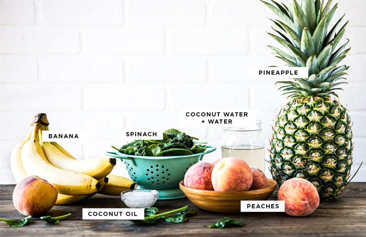 labeled ingredients for a pre workout smoothie including banana, coconut oil, spinach, peaches, coconut water + water and pineapple.