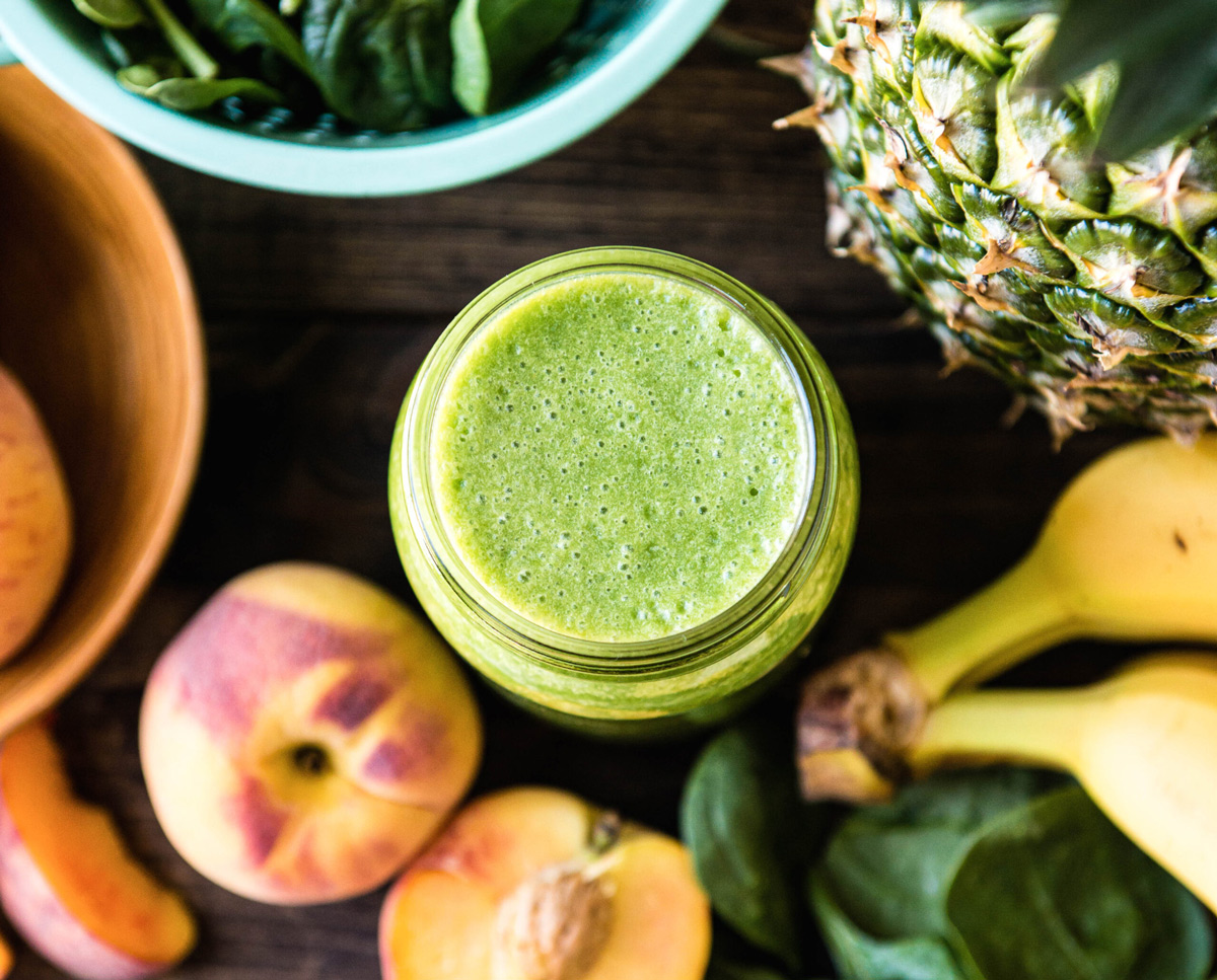 Jar filled with a green pre-workout smoothie surrounded by fresh produce with banana, spinach, and pineapple.