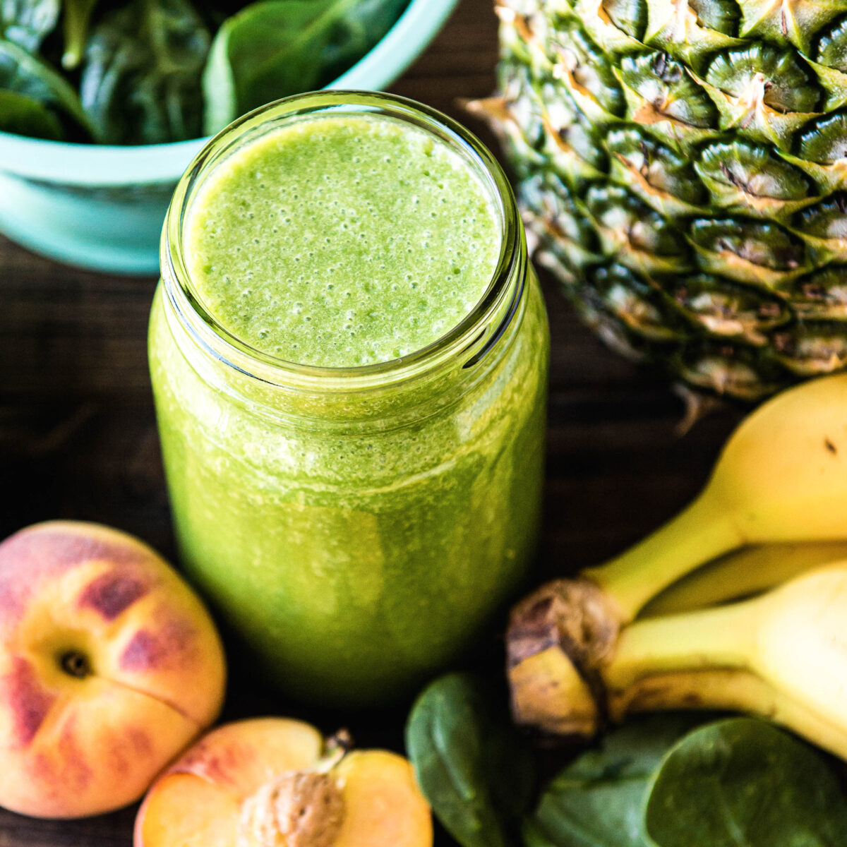 Jar of green smoothie surrounded by fruits and greens.
